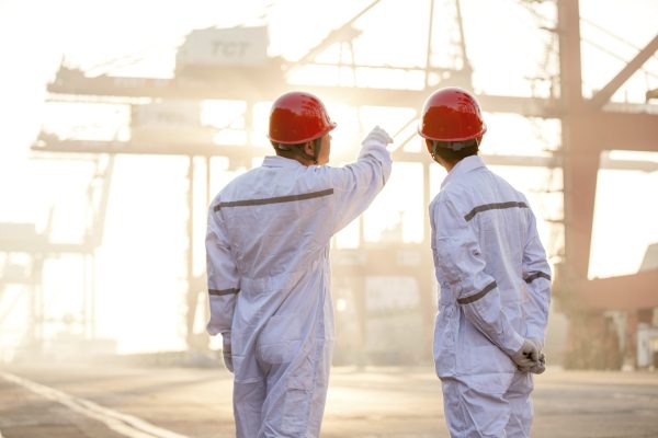 Two professionals discussing work at a bustling industrial port at sunrise.